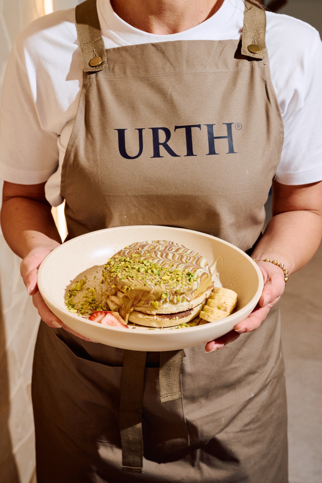 A URTH team member holding a plate of pistachio pancakes
